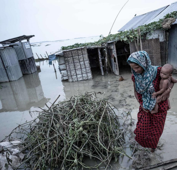 climate-sanitation-health-paper-cover A woman holding a baby walking in a flooded soil