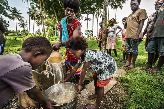 Kids holding a bucket while woman pours water into the bucket
